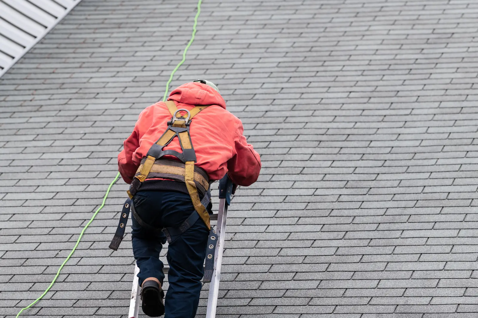 Roofer wearing a safety harness while inspecting a shingle roof